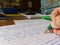 A teacher marking an exam paper at a desk with green pen in hand