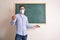 Teacher with mask explaining lesson in front of green blackboard