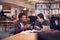 Teacher With Mature Male Adult Student Sitting At Table Working In College Library