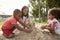 Teacher At Montessori School Playing With Children In Sand Pit