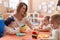 Teacher and preschool students learning to eat sitting on table at kindergarten