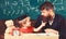 Teacher and pupil in mortarboard, chalkboard on background. Naughty child concept. Kid cheerful distracting while