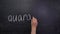 The teacher`s hand writes the word QUARANTINE on a chalkboard.