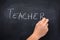 Teacher`s hand writing the word teacher on a blackboard