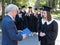 The teacher shakes hands with the student and presents the diploma outdoors. A group of university graduates.