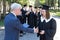 The teacher shakes hands with the student and presents the diploma outdoors. A group of university graduates.