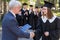 The teacher shakes hands with the student and presents the diploma outdoors. A group of university graduates.