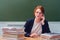 Teacher sits at a desk and speaks by phone at the school blackboard