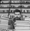 Teacher or student with beard sits at table with glasses, defocused. Man on strict face between piles of books, while