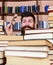 Teacher or student with beard wears eyeglasses, sits at table with books, defocused. Man on surprised face between piles