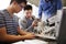 Teacher With Two Male College Students Building Machine In Science Robotics Or Engineering Class