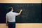 Teacher wearing face mask writing on a blackboard in a classroom. Covid situation, pandemic, new normal