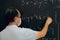 Teacher wearing mask writing equations on a blackboard. Covid situation, pandemic, new normal