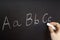 Teacher is writing letter of alphabet on blackboard with chalk.