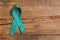 Teal awareness ribbon on wooden background, top view with space for text. Symbol of social and medical