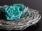 Teal and blue paper rose flower blooms on gray wood coiled up against a slate black background.  Pretty home decor