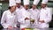 Team of chefs watching head chef slicing vegetables