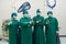 A team of four surgeons dressed in scrubs, standing amid the sterile environment of an operating room, they pose for a moment of