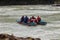 A team of people rafting in equipment, lifejackets and yellow helmets on a blue inflatable boat along a mountain river with rapids