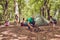 Team work. Young bearded male tourist in a hat is setting campfire, other set on a tent, ladys are unoacking and organizing the m