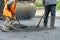 A team of workers with shovels is working on laying new asphalt. Road repairs. Workers with tools next to a roller asphalt stacker