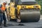 A team of workers with shovels is working on laying new asphalt. Road repairs. Workers with tools next to a roller asphalt stacker