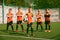Teammates. Athletic boys in junior soccer team standing together at grass sport field. Football players in orange-black