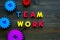 Teamwork concept. Text teamwork lined with colored letters near toy gears on dark wooden background top view copy space