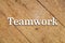 `Teamwork` white text on a wooden background.