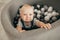 Tearful toddler stands in basket with small balls and cries.