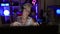 Tech-savvy, grey-haired senior woman enthrals gaming world as she streams live video call, gamepad in hand, from her darkly lit