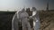 Technical team of lab employees in hazmat suits sampling and examining vegetation and soil from field near of power plant -