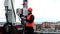 Technical worker male in the bright protective clothing works on the roof near the antenna and takes notes in notebook