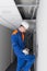 A technician in a blue uniform and a white helmet, has wired the wifi router in a hidden false ceiling system and verifies the