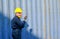 Technician or engineer with blue uniform and yellow helmet use walkie-talkie to contact with co-worker in cargo container shipping