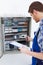 Technician holding clipboard while examining fusebox