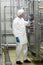 Technician in white coveralls and cap controlling industrial process in plant