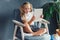 Technologies, people concept - young blondy girl sitting on a chair and watching the tablet or surfing the net and smiling