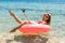 Technology and people concept - smiling young woman or teenage girl makes selfie on inflatable donut with smartphone on beach