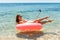 Technology and people concept - smiling young woman or teenage girl makes selfie on inflatable donut with smartphone on beach