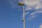 Technology view of light sensor on street lighting pole on blue sky with rare white clouds background.
