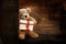 Teddy bear brings a Christmas present decorated with a red ball chain, dark rustic wooden background with copy space