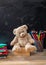 Teddy bear and colorful pencils and notebooks on blackboard background, copy space