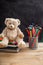 Teddy bear and colorful pencils and notebooks on blackboard background, copy space