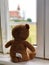 A teddy bear doll watching outside through a window