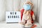 Teddy bear doll wearing mask backpack and holding lightbox with text NEW NORMAL on wooden background, copy space, Quarantine 2020