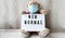 Teddy bear doll wearing mask backpack and holding lightbox with text NEW NORMAL on wooden background, copy space, Quarantine 2020