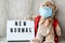Teddy bear doll wearing mask backpack and holding lightbox with text NEW NORMAL on wooden background, copy space, Quarantine 2020