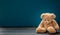 Teddy bear sad, sitting on the wooden floor, blue empty room background, copy space