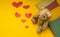 A teddy bear sits near books on a yellow background of scattered hearts